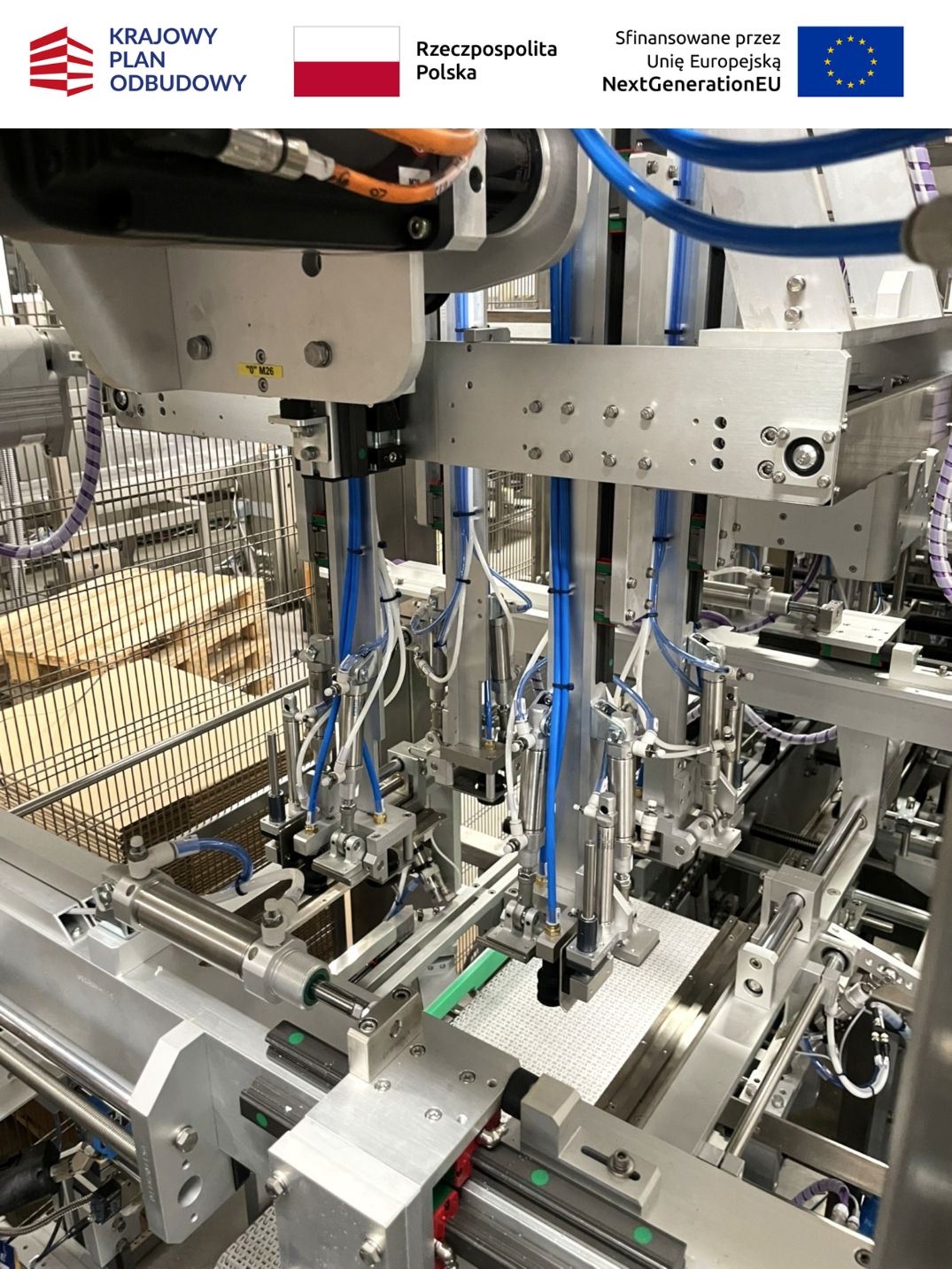Zbliżenie na wewnętrzny mechanizm pneumatyczny maszyny pakującej Ulma z widocznymi siłownikami, niebieskimi przewodami ciśnieniowymi i precyzyjnymi prowadnicami.