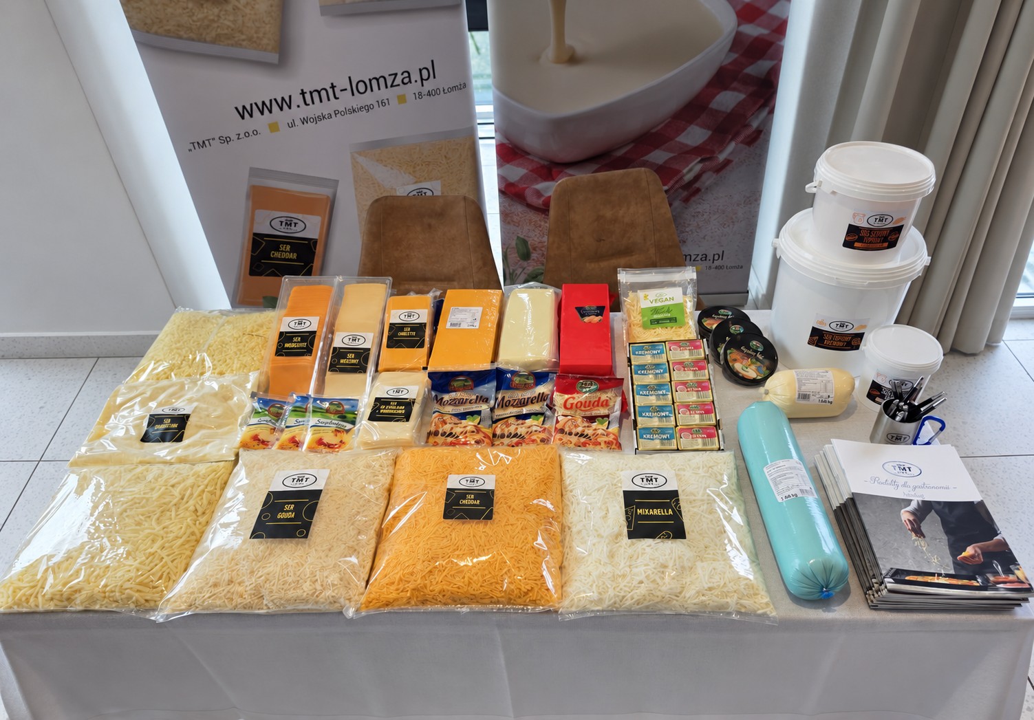 Stoisko TMT Gastro podczas targów SOT Chorzów 2026, prezentujące szeroki asortyment serów do gastronomii, w tym sery tarte, w plastrach, mozzarella, gouda, cheddar oraz sosy serowe.